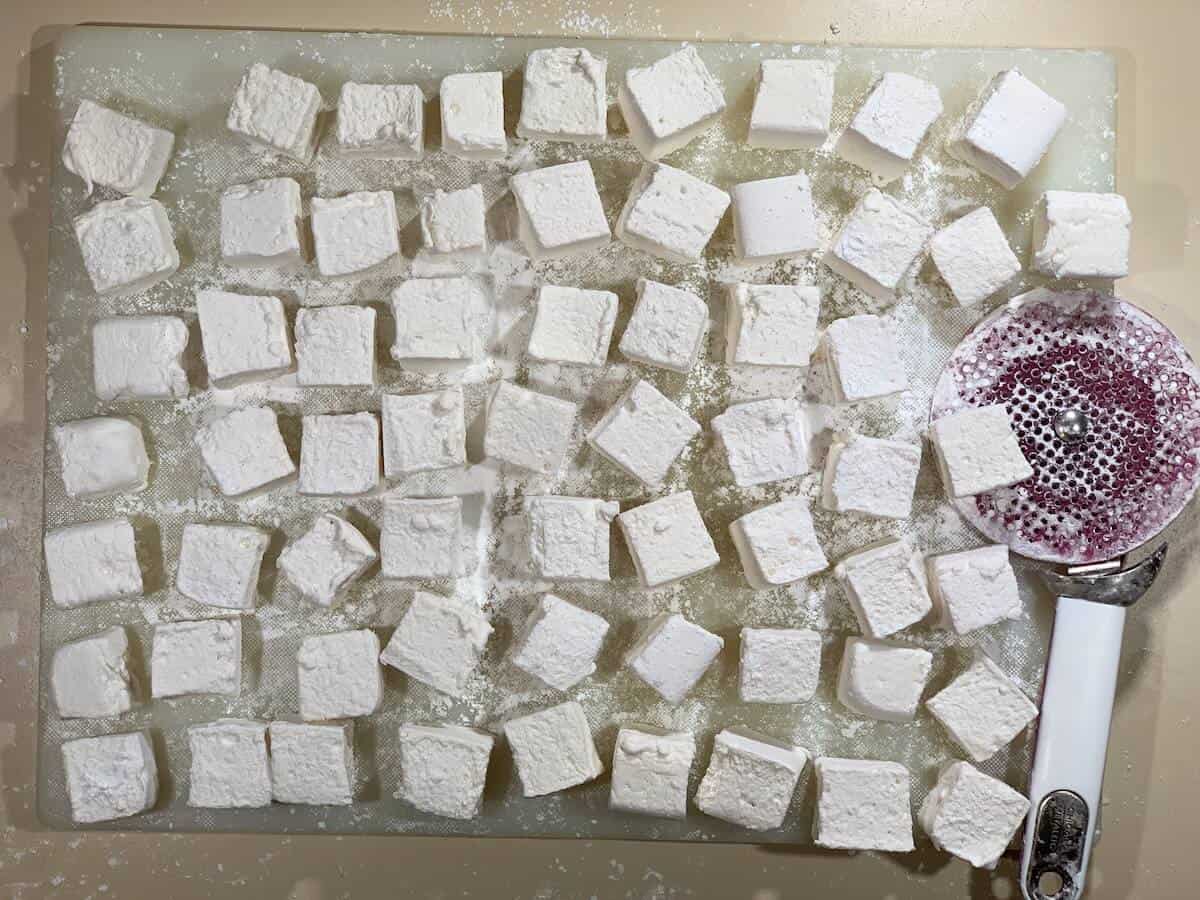 Whiskey marshmallows on cutting board with cutter.