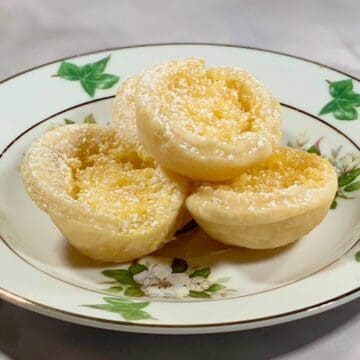 Mini Lemon Tartlets stacked on a white plate with green leaves.