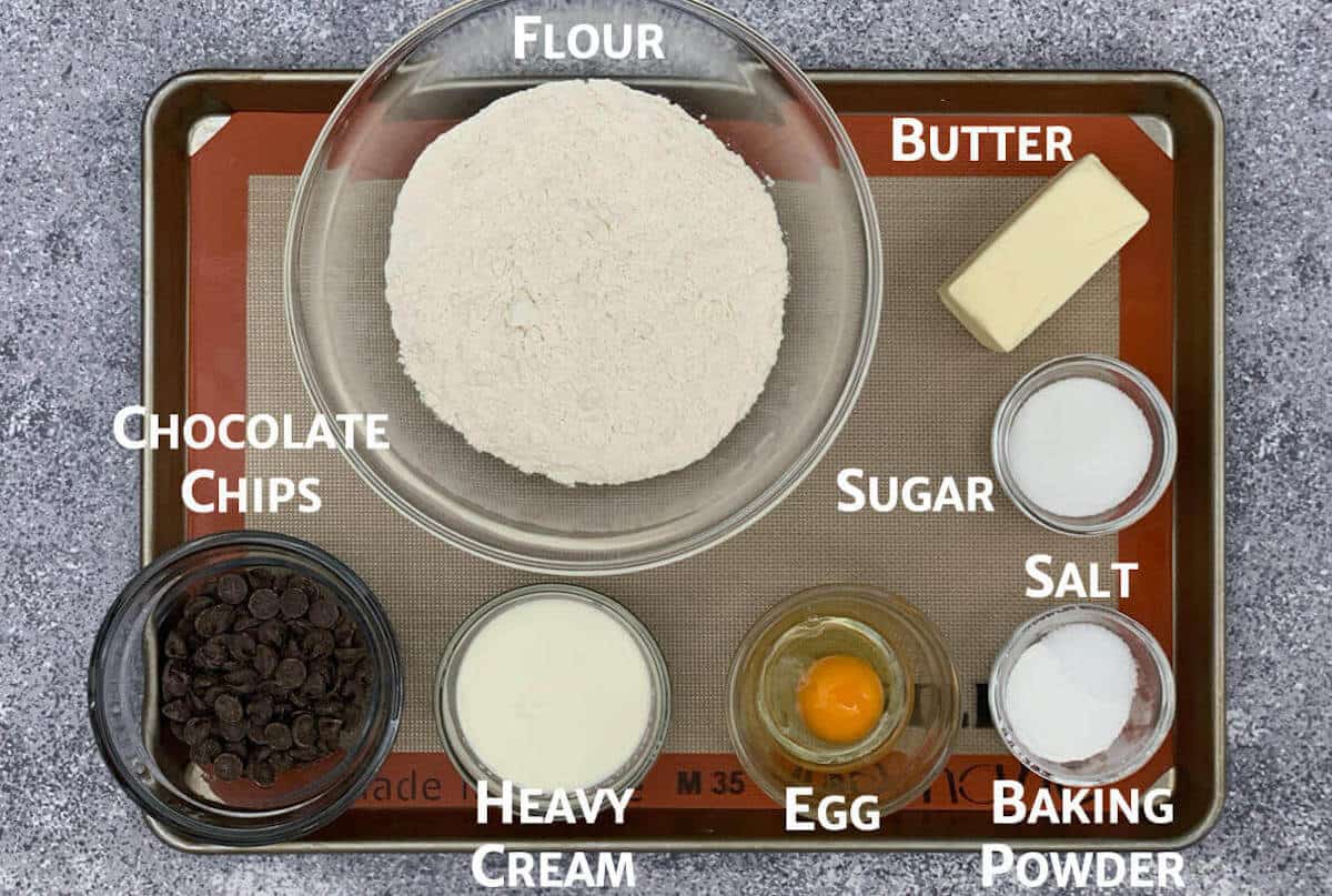 Chocolate chip cream scones ingredients portioned into glass bowls on a baking pan.