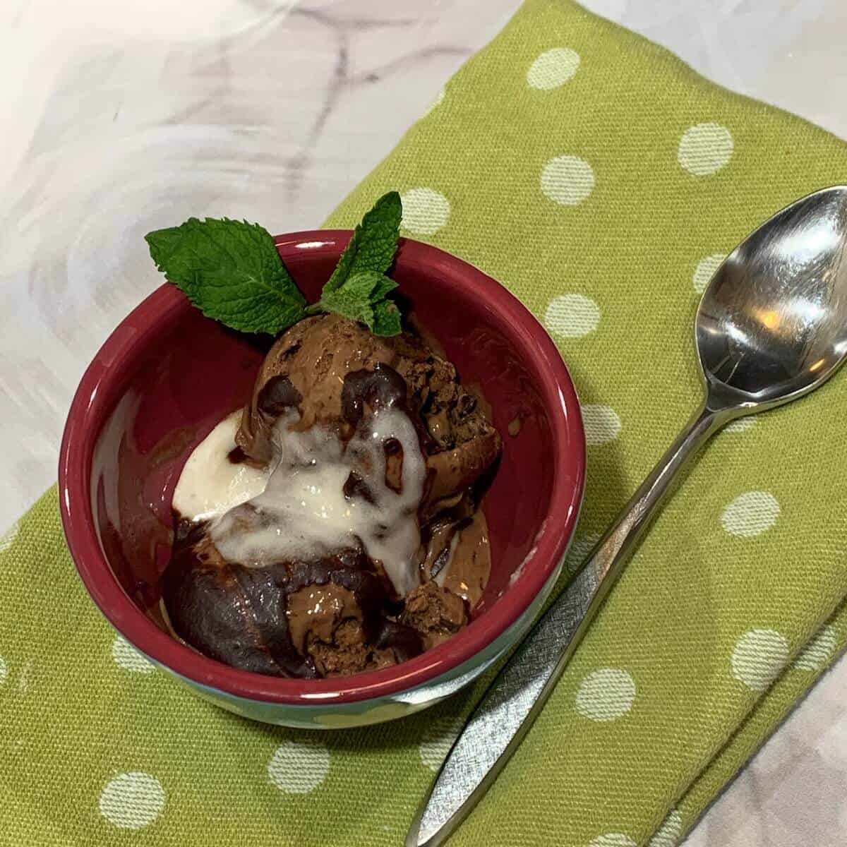 Chocolate Mint Chip gelato sundae in bowl on a green spotted towel next to a spoons.