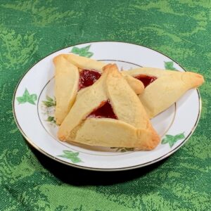 Raspberry Hamantaschen cookies stacked on a white plate with green trim on a green background.