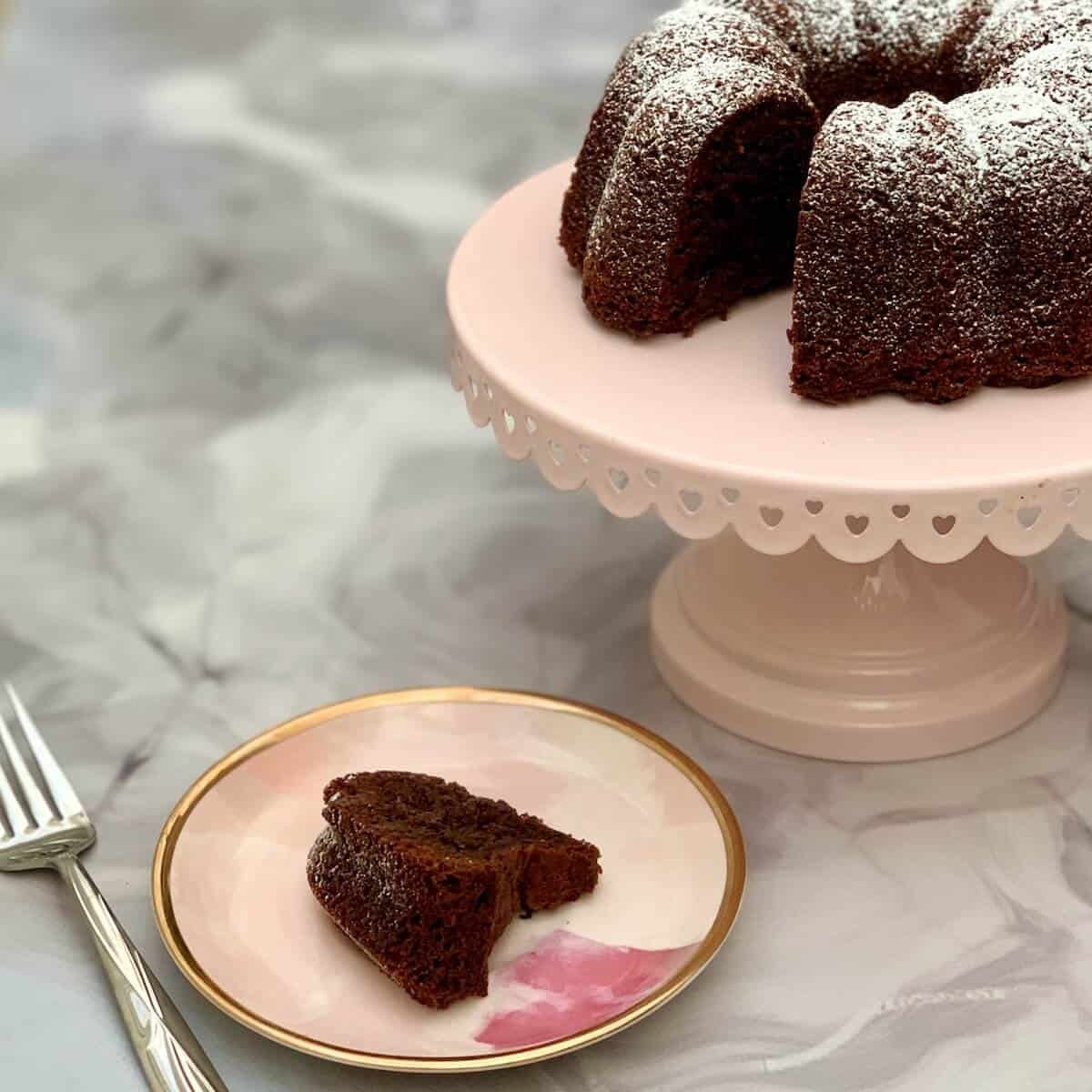 Kahlua Cake slice on a pink plate on front of cake on pink cake stand.