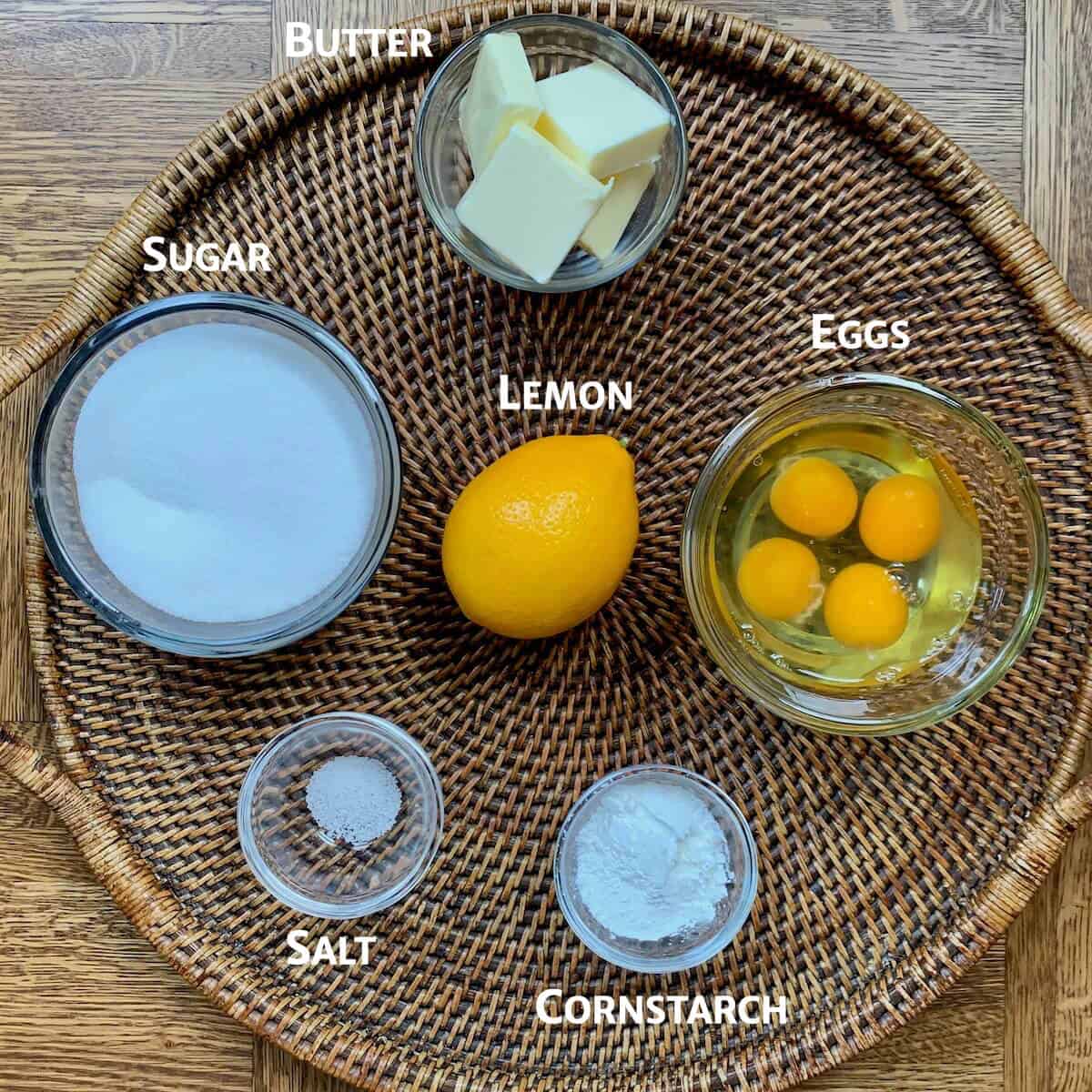 Lemon tartlet ingredients portioned in glass bowls on a woven tray.