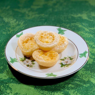 Lemon tartlets stacked on a white plate atop a green background.