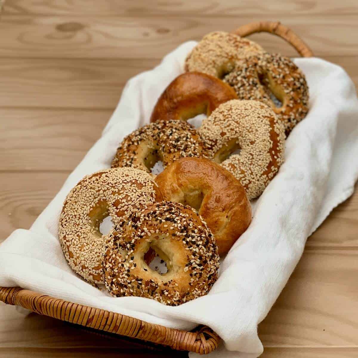 Assorted sourdough bagels on a white towel in a basket.