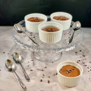 Three ramekins of Dairy-Free Chocolate Mousse on a glass cake stand with spoons and 1 in front.