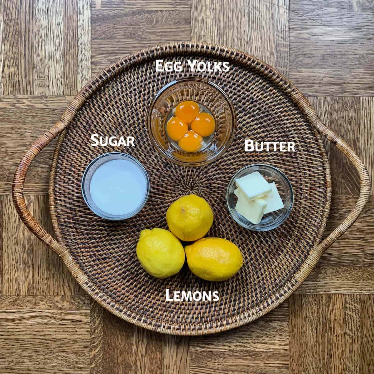 Lemon curd ingredients portioned into glass bowls on a woven tray.