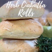 Sourdough Herb Ciabatta Rolls stacked next to rosemary with rolls on a green spotted towel behind Pinterest banner.