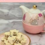 White Chocolate Marshmallow Pecan Fudge plated stacked on a pink plate beside a pink teapot Pinterest banner.