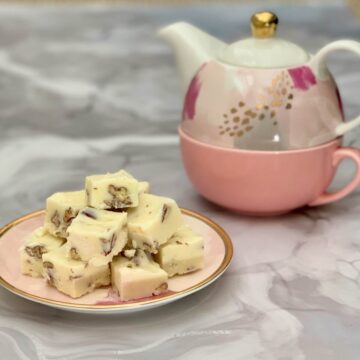 White Chocolate Marshmallow Pecan Fudge plated stacked on a pink plate beside a pink teapot.