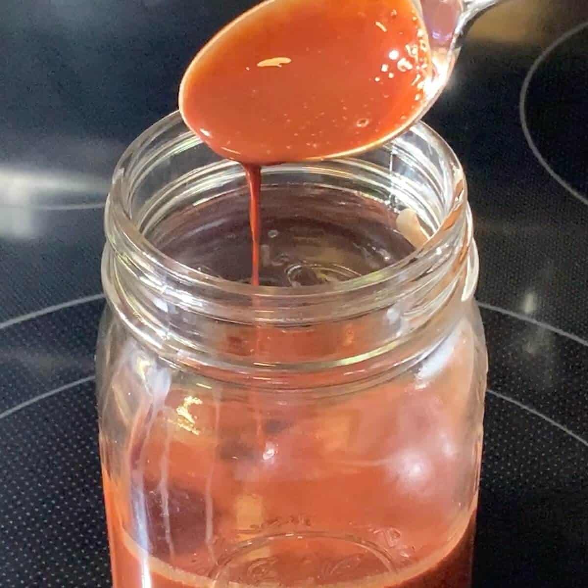 Chocolate syrup dripping from spoon into a jar.