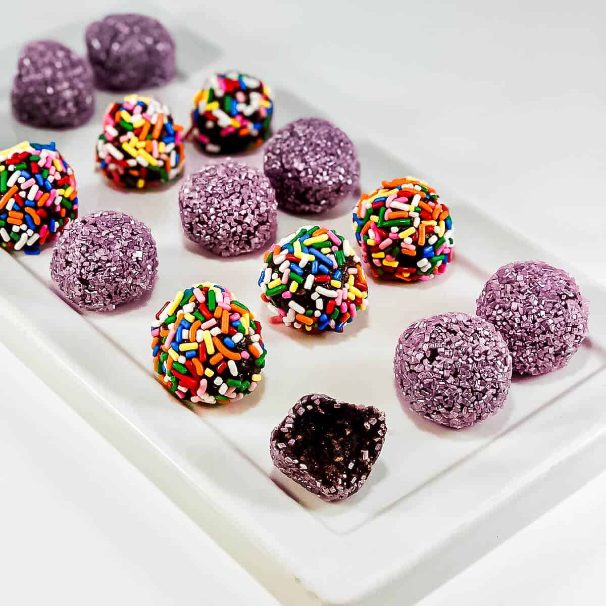 Rum balls with different topping with one bitten on a white plate.