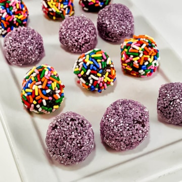 Rum balls with different topping on a white plate.