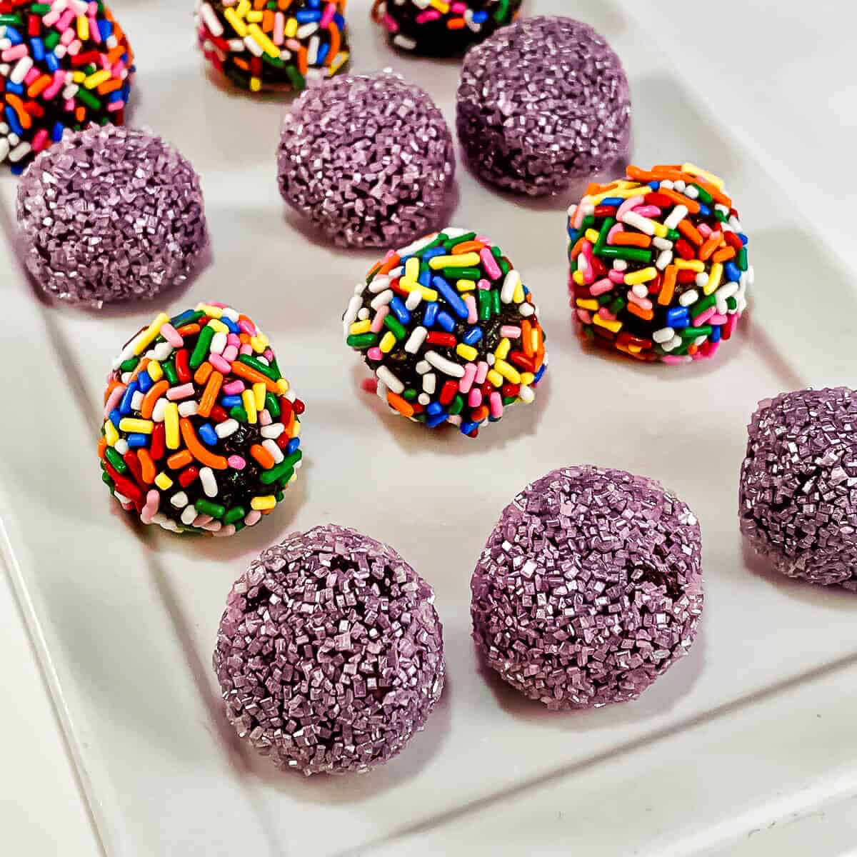 Rum balls with different topping on a white plate.