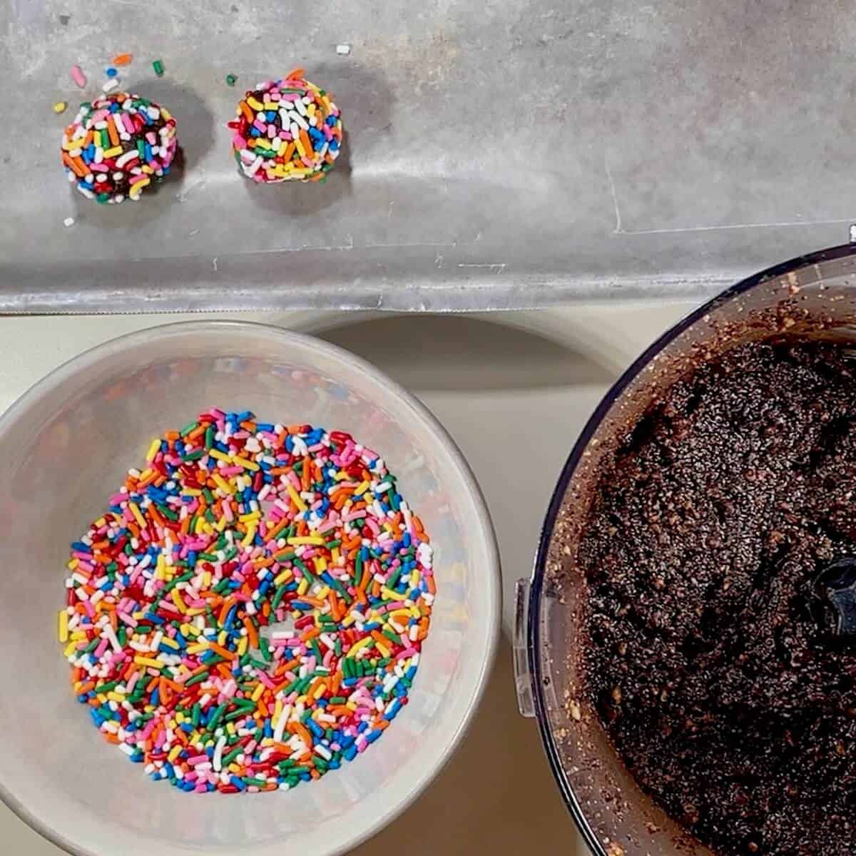 Finished rum balls on a tray with bowl of sprinkles & dough.