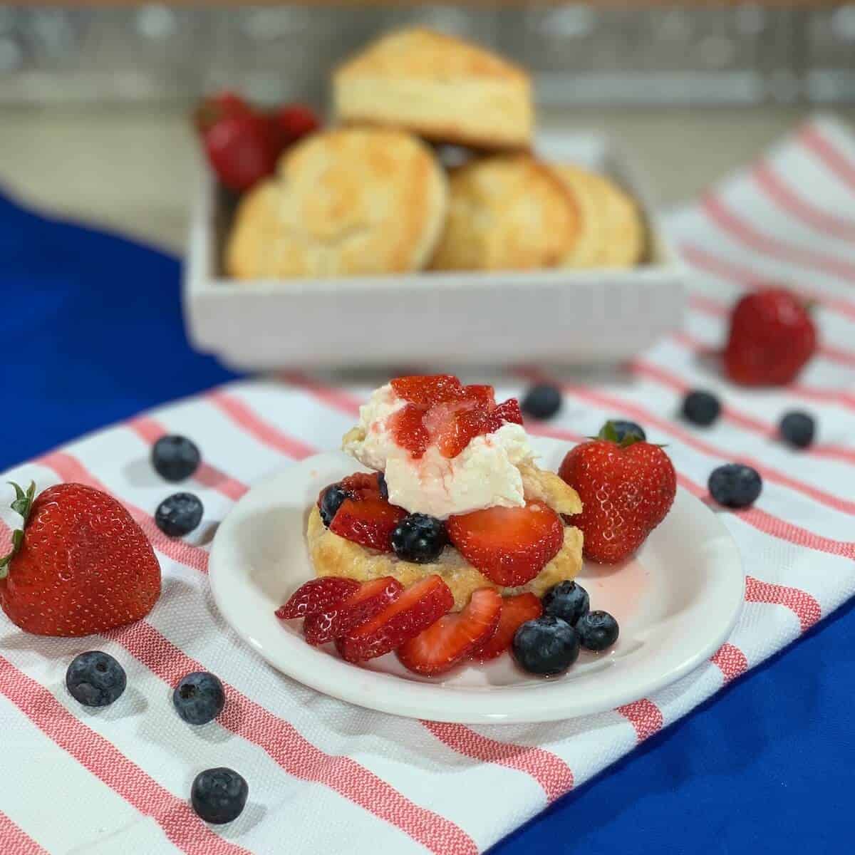 Strawberry Blueberry Shortcake plated on red striped towel with stacked shortcakes in background.