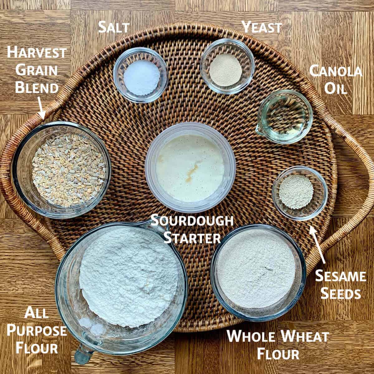 Multigrain Sourdough Sandwich Bread ingredients portioned in glass bowls on a woven tray.