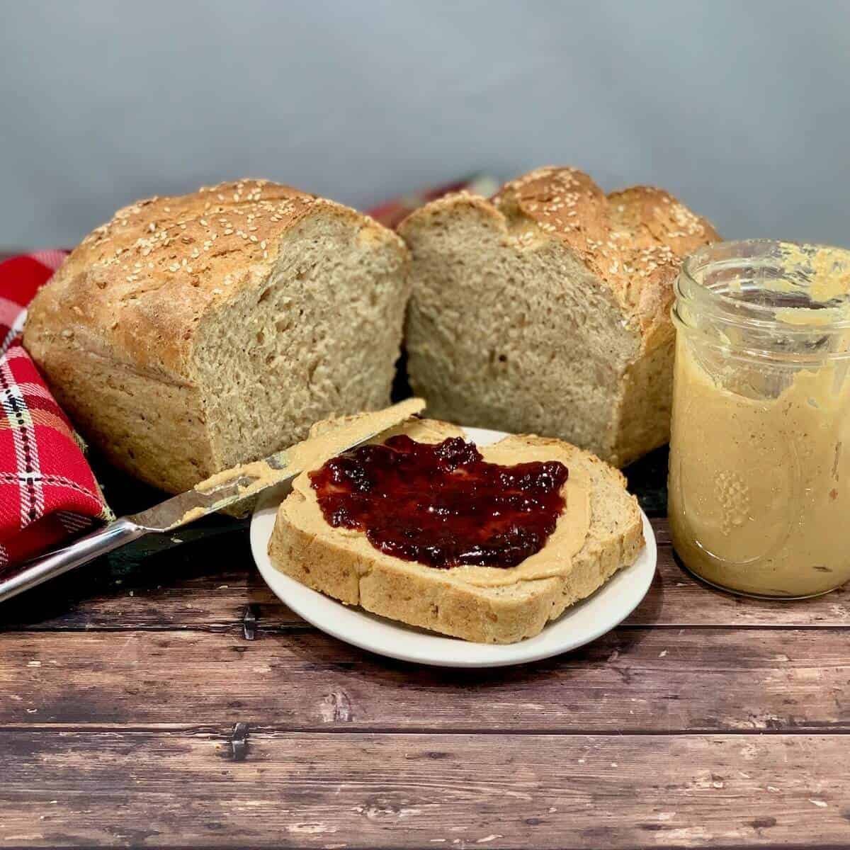 Sliced Multigrain Sourdough Sandwich Bread loaf with open faced peanut butter & jelly sandwich.