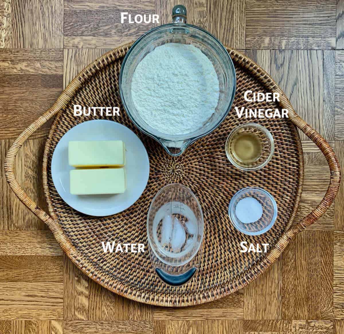 Pie crust ingredients in glass bowls on a wooden tray.