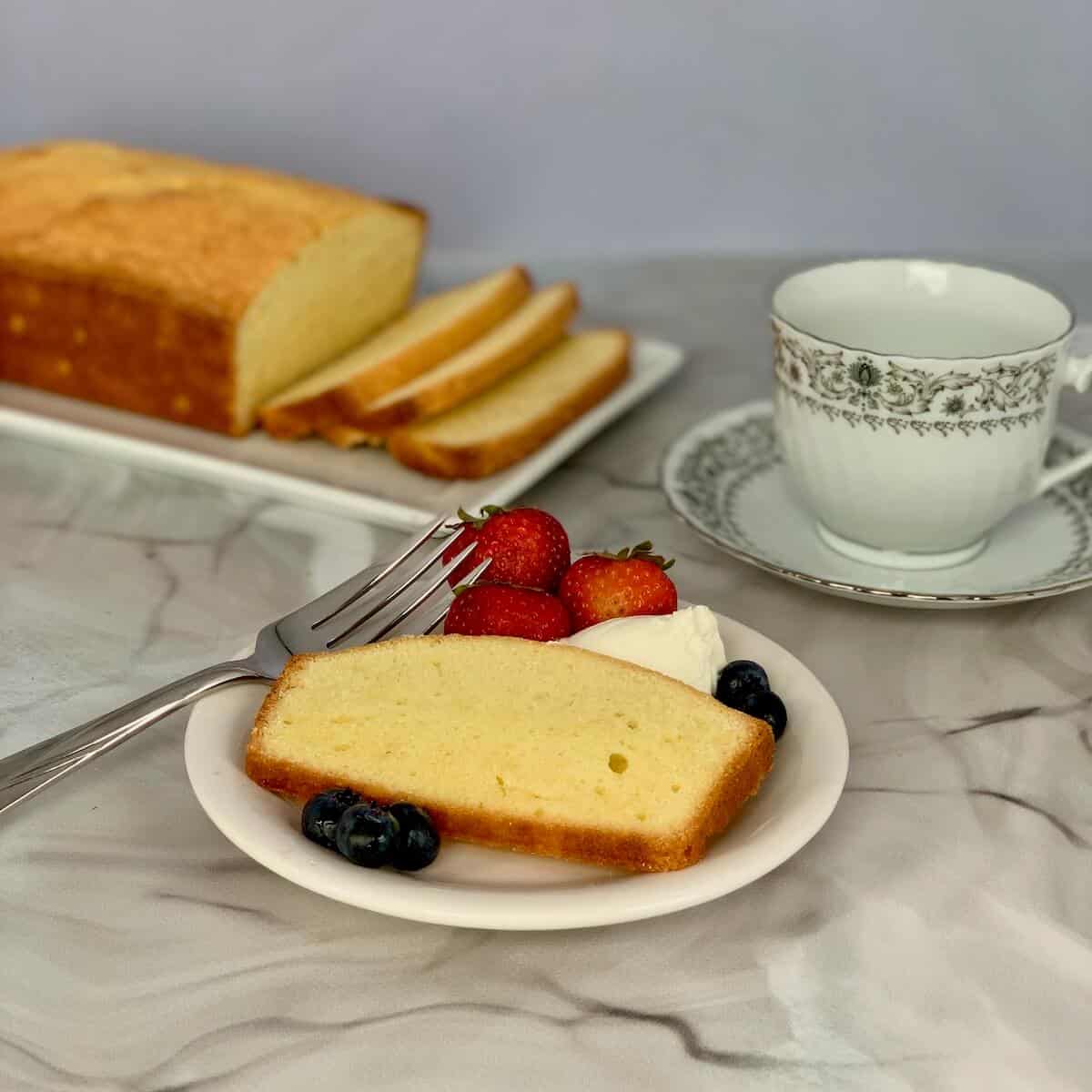 Orange Vanilla Pound Cake plated sliced with cream and berries, sliced loaf & cup in background.