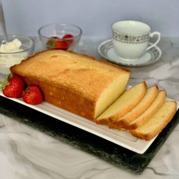 Orange Vanilla Pound Cake loaf sliced with cream, strawberries, & teacup.