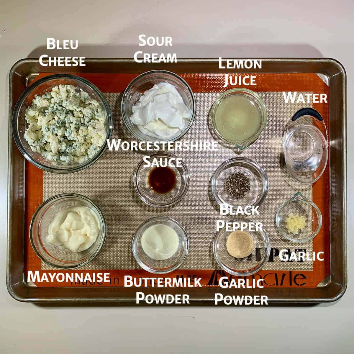 Buttermilk blue cheese dressing ingredients portioned into glass bowls on a baking pan.