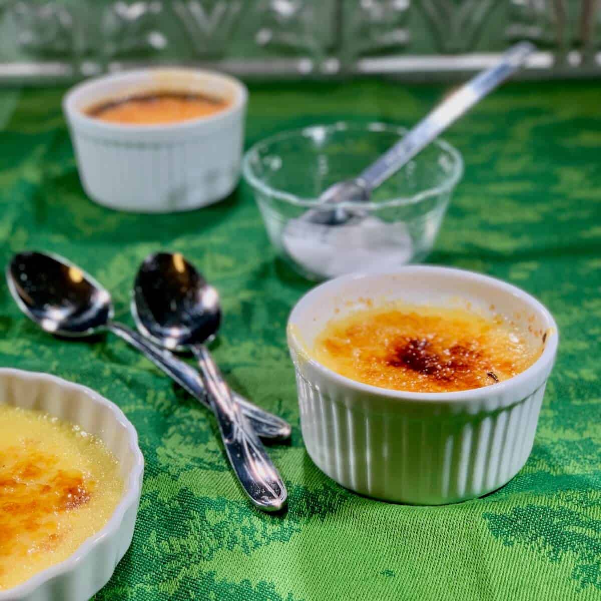 Creme Brulee on a green towel with spoons and sugar in background.