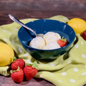 Lemon Sherbet scooped in blue bowl on green towel with strawberries & lemons.