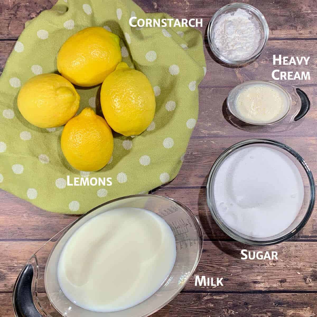 Whole Lemon Sherbet ingredients in bowls & lemons on a green towel all on a wood backdrop.