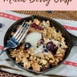 Mini Skillet Berry Crisp on a red & white striped towel with fork & scoop of vanilla ice cream surrounded by blueberries on a wooden tray Pinterest banner.