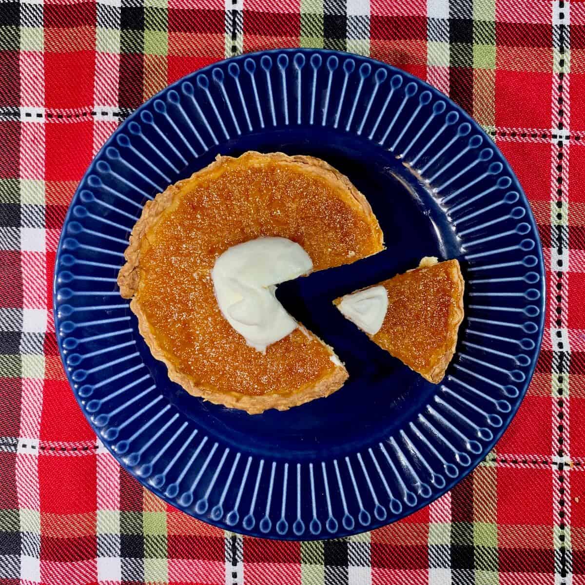 Treacle Tart sliced & plated on a blue plate with a plaid background from overhead.