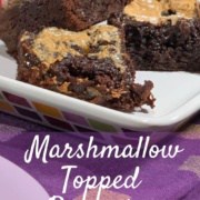 Marshmallow topped brownies on a white plate with more on a multicolored checked plate behind on a purple checked towel Pinterest banner.