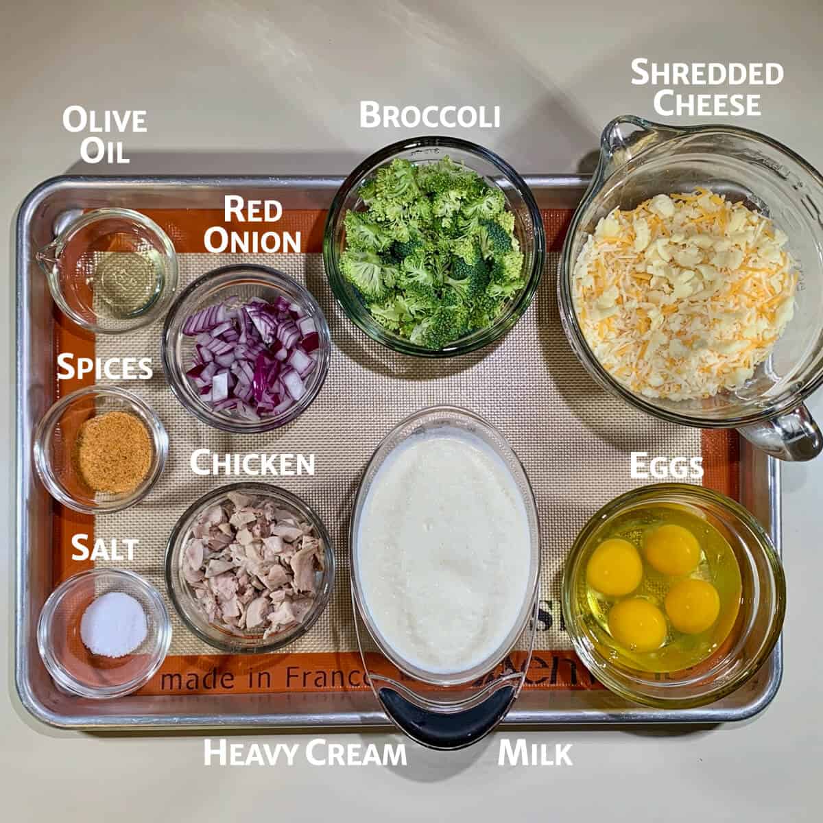 Chicken Broccoli Quiche ingredients portioned into glass bowls on a baking pan.