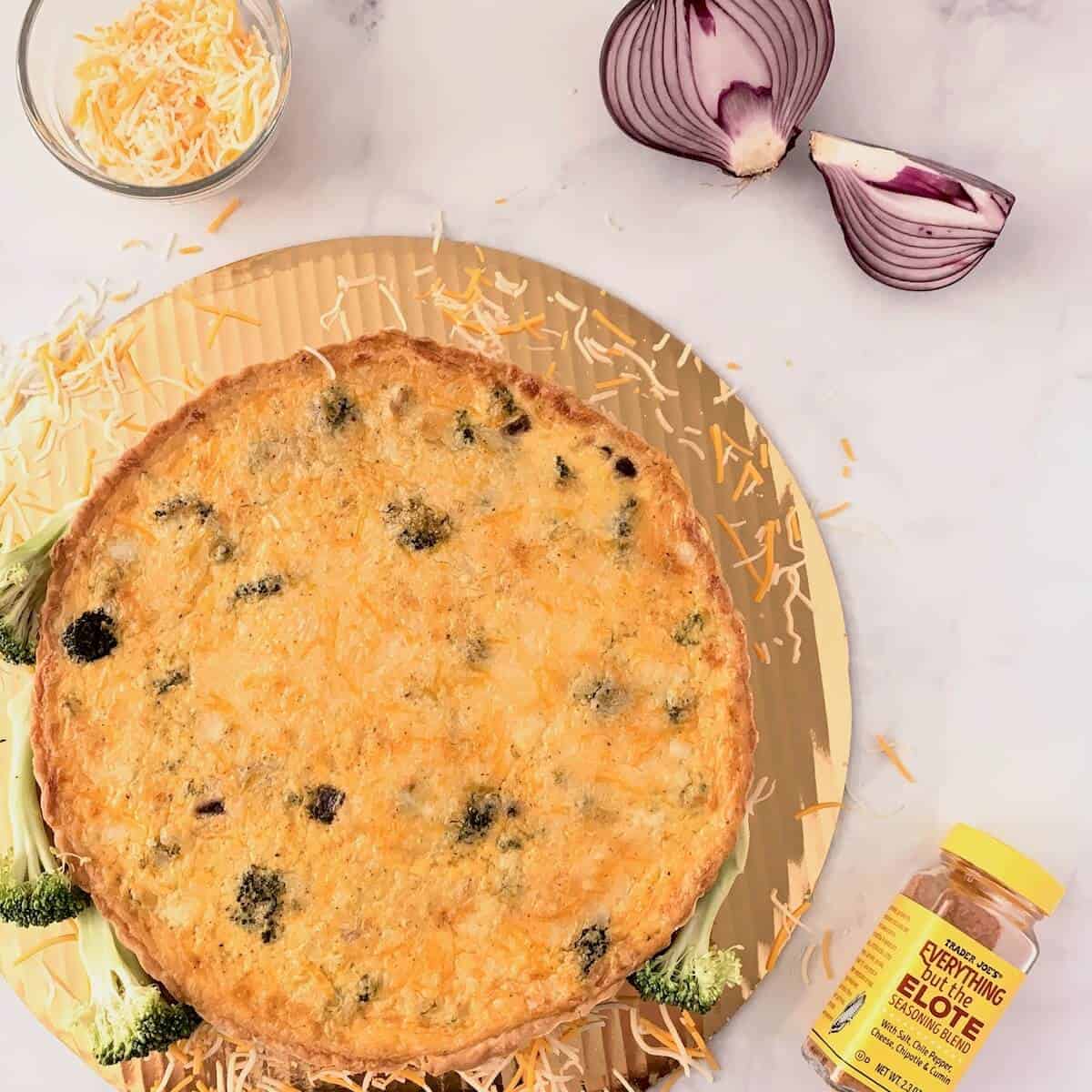 Chicken Broccoli Quiche on a gold base with cheese, seasonings, & red onion from overhead.