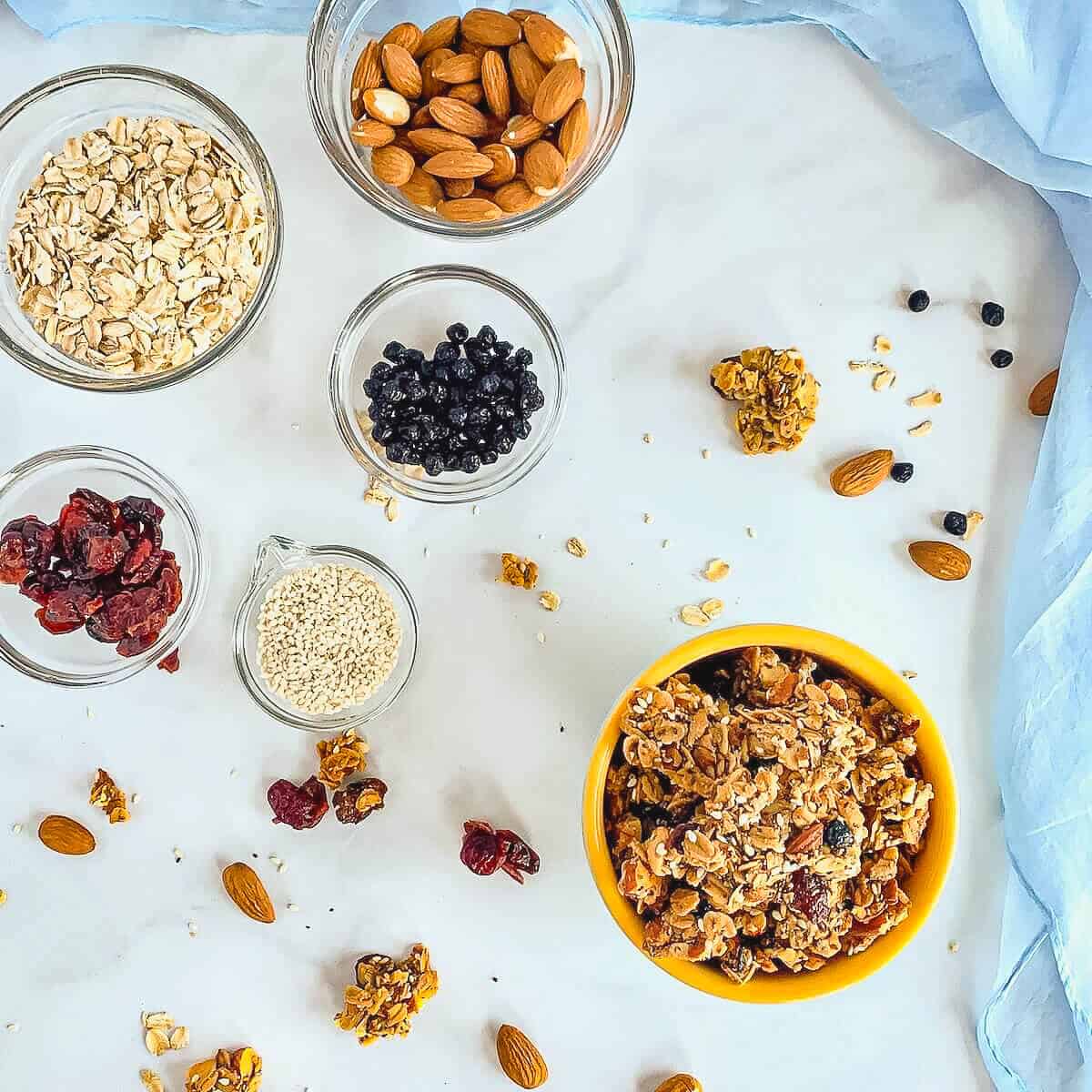 Granola in a bowl next to ingredients portioned into glass bowls from overhead.
