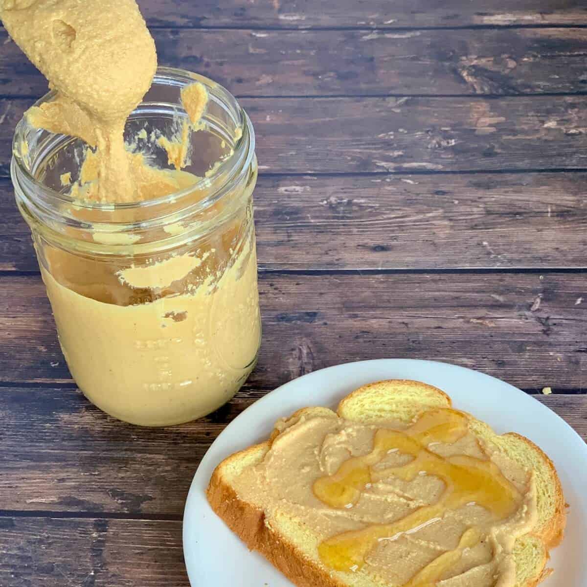 Peanut Butter jar with dripping spoon next to open face honey sandwich.