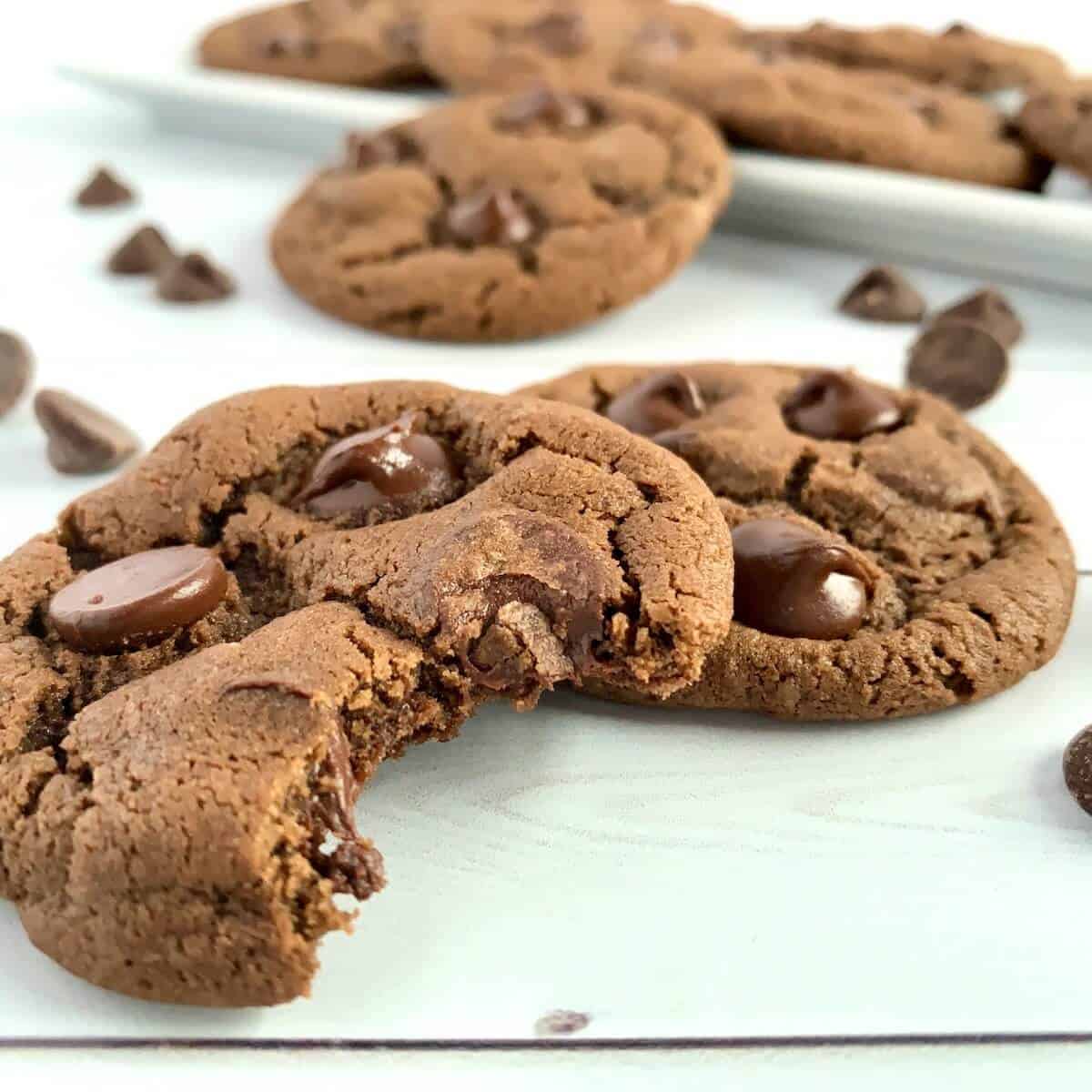 Bitten Chocolate Chocolate Chip cookies with white tray of cookies behind.