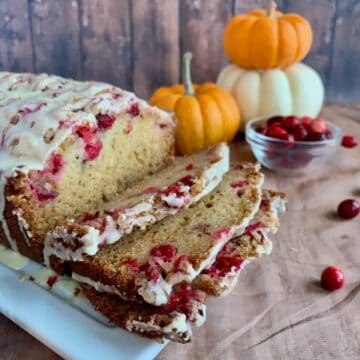 Glazed Orange Cranberry Bread sliced on a white plate with pumpkins & cranberries.