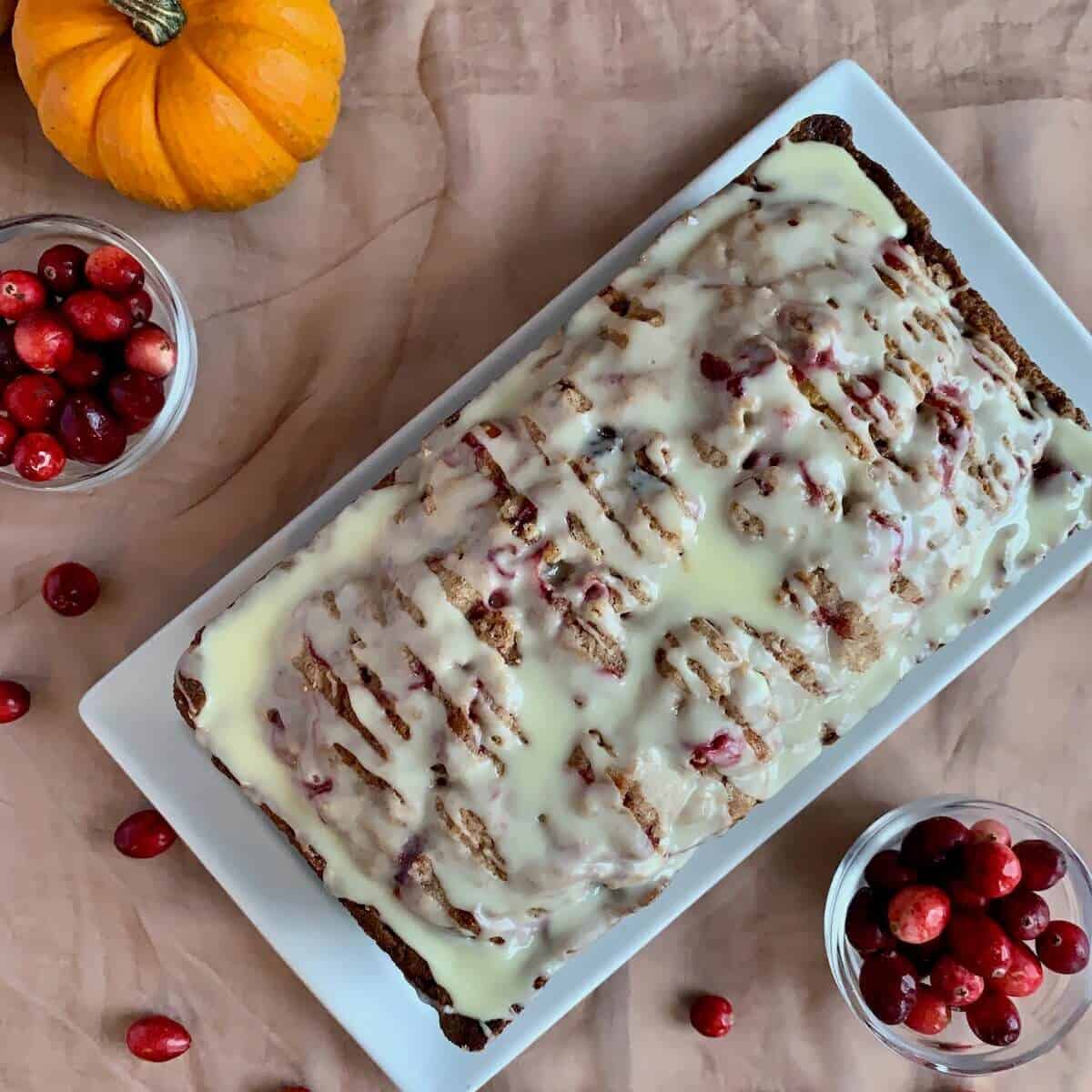 Glazed Orange Cranberry Bread on a white plate with pumpkins & cranberries from overhead.