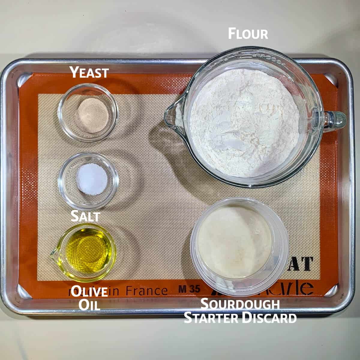 Sourdough focaccia ingredients portioned into glass bowls on a baking tray.