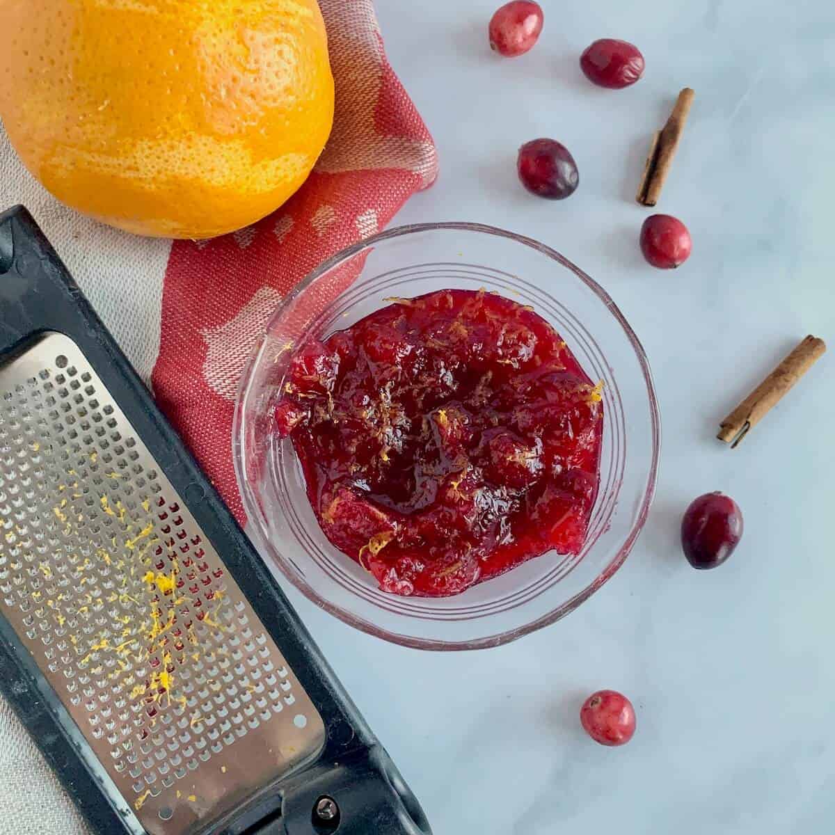 Orange Cranberry Sauce in a glass bowl with tools and ingredients from overhead.