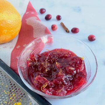 Orange Cranberry Sauce in a glass bowl with tools and ingredients.
