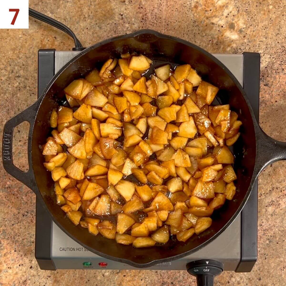 The cooked apple filling in a cast-iron skillet on a hot plate.