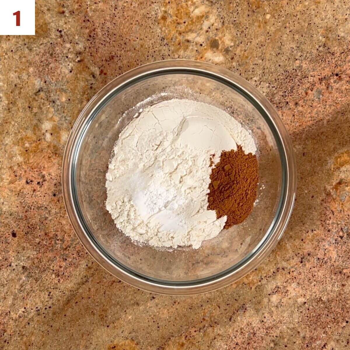 Flour, apple spice mix, baking powder, baking soda, and salt in a glass bowl from overhead.