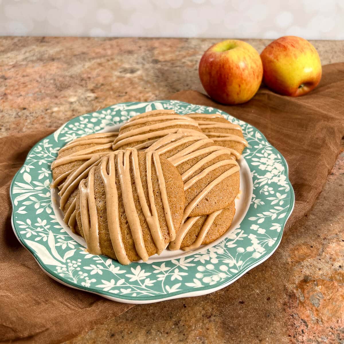 Apple spice cookies stacked on a glass stand with a bite out of the top one.