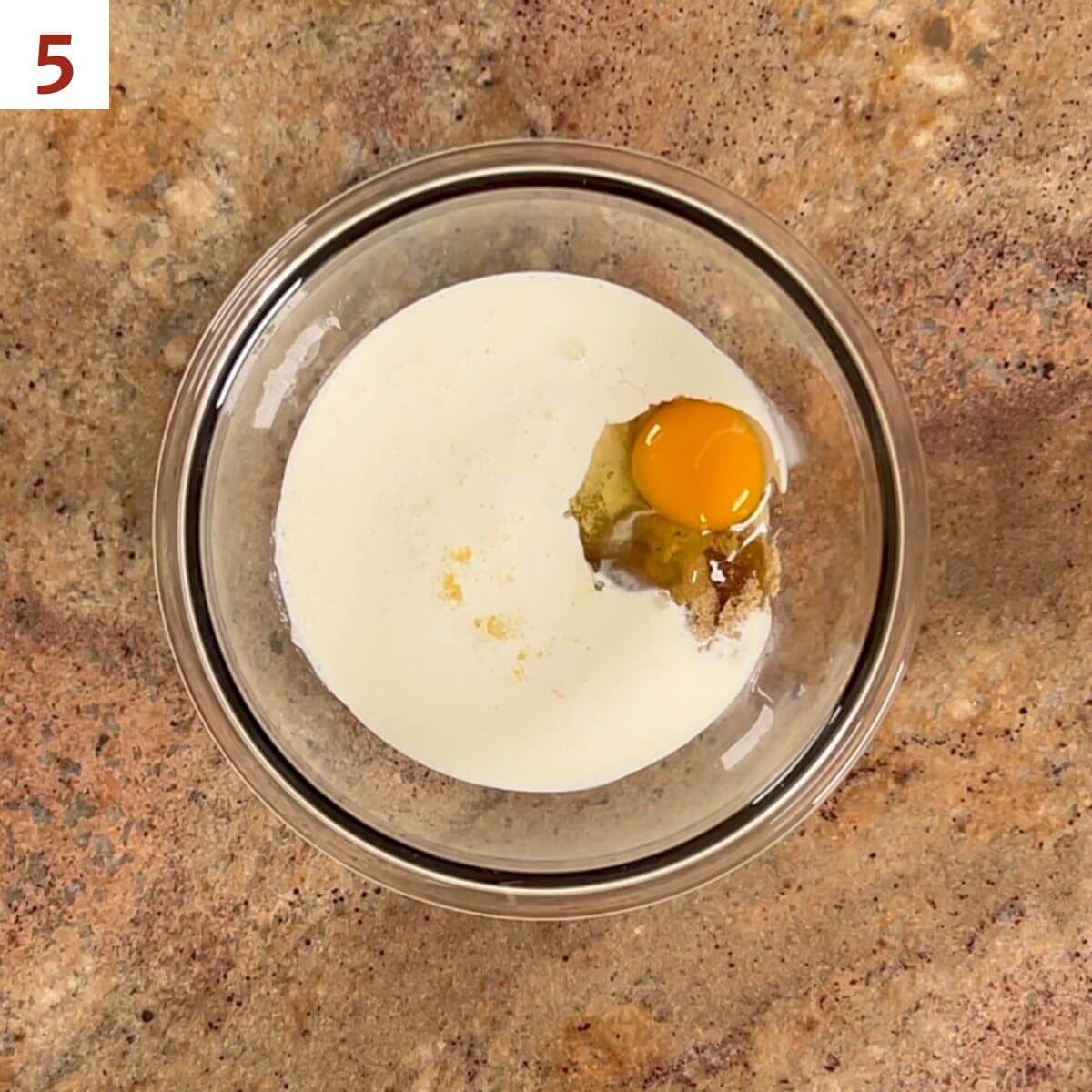 Heavy cream, maple syrup, brown sugar, and egg in a glass bowl from overhead.