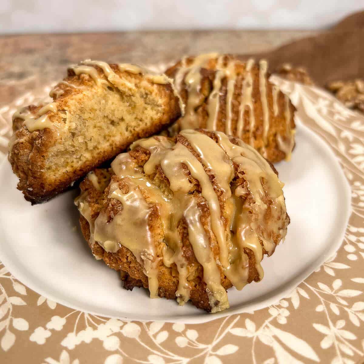 Maple walnut scones stacked on a white plate with a brown flowered edging with one cut in half.