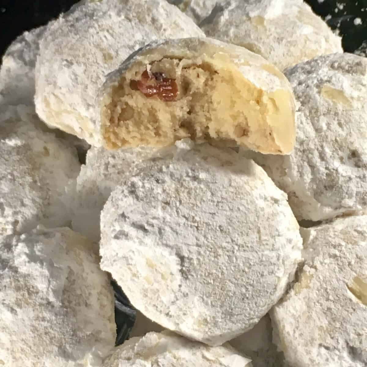 Closeup of a bitten pecan snowball cookies stacked on others.