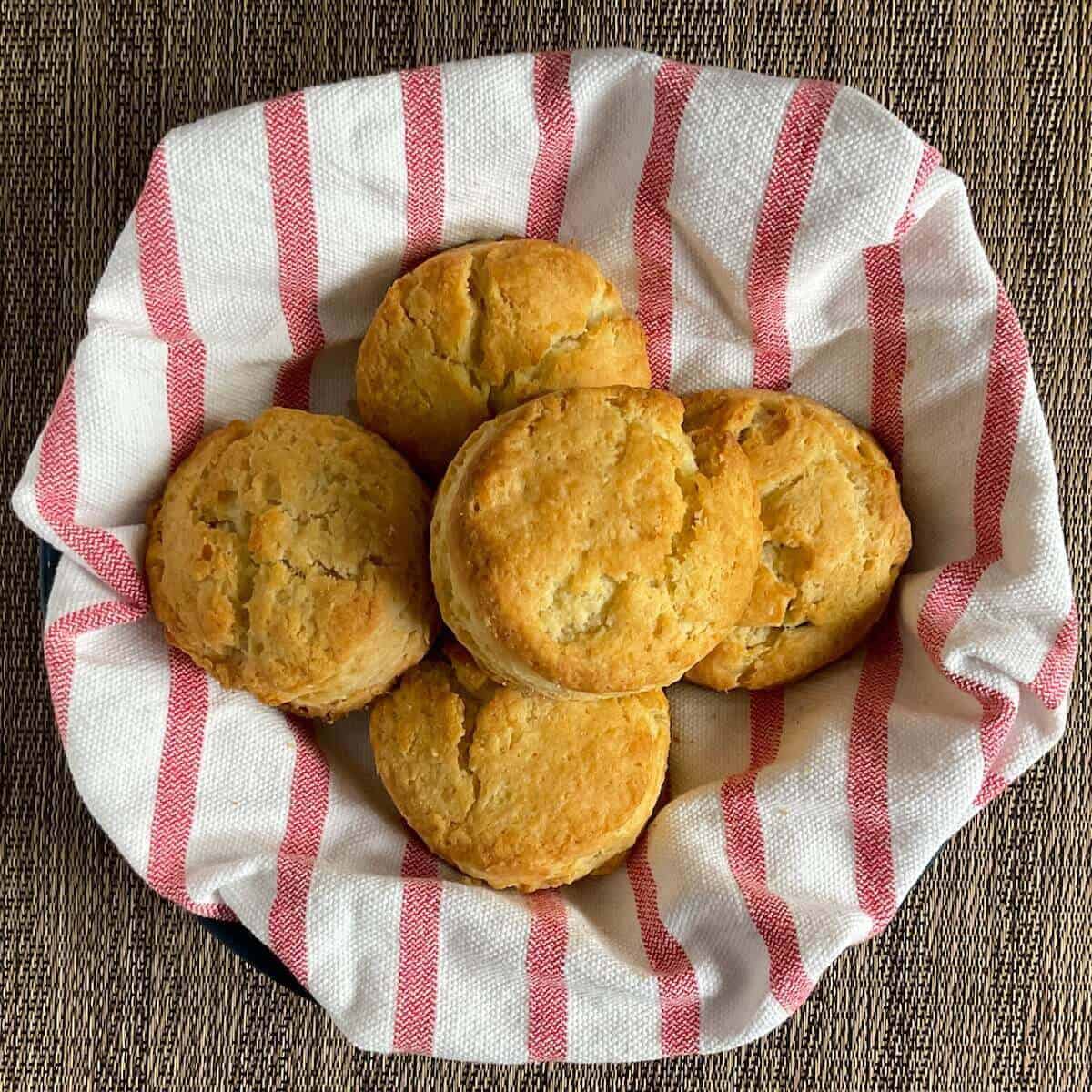 Biscuits stacked on a red & white striped towel nestled in a bowl from overhead.