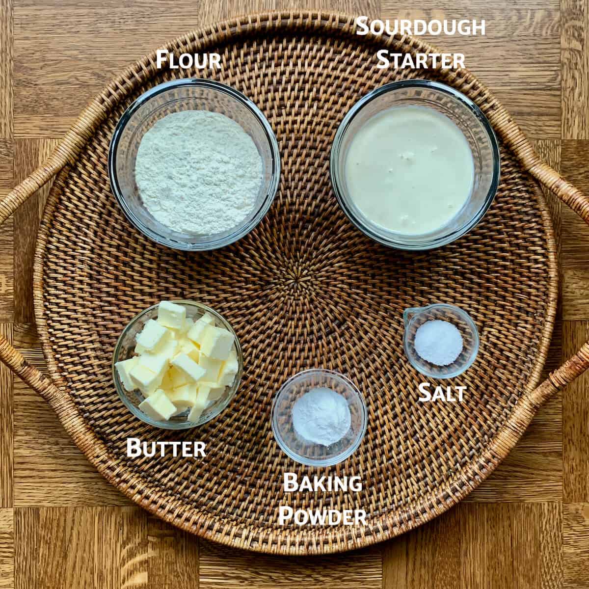 Sourdough biscuit ingredients portioned into glass bowls on a wooden tray from overhead.